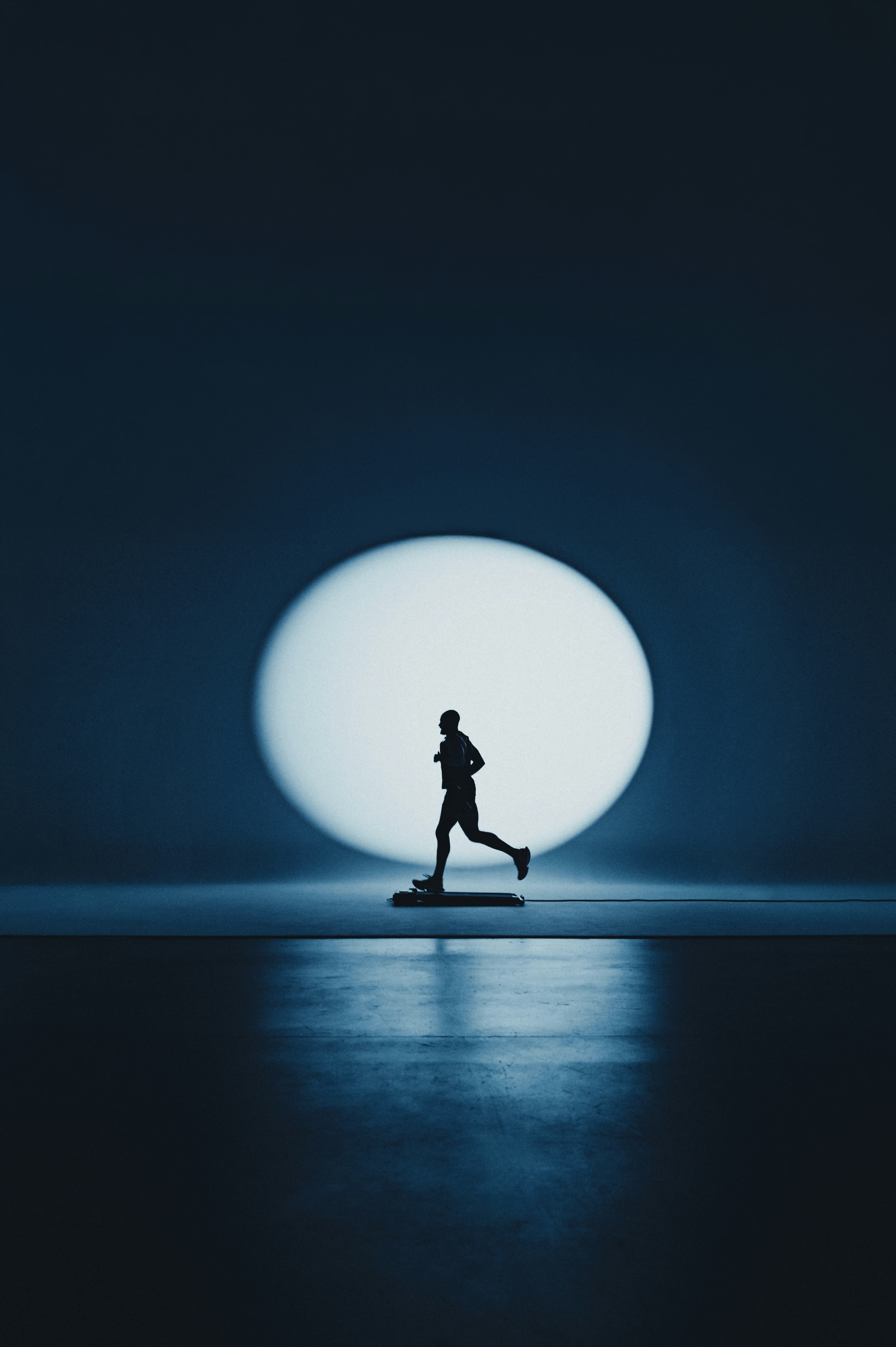 Silhouette of a runner on a treadmill in a circular spotlight against a dark blue background